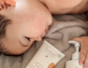 baby laying on bed surrounded by Babo Botanicals Bath Products for baby hair