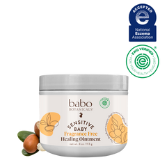 A jar of babo Botanicals Sensitive Baby Fragrance Free Healing Ointment on a white background, accompanied by two certification logos (National Eczema Association and Organic Versed) and a small cluster of almonds and green leaves at the base of the jar.